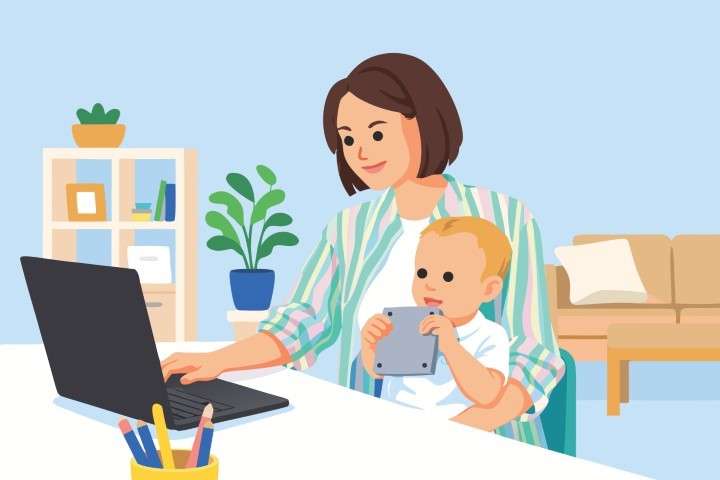 Mother working on her laptop at home while holding her small baby.