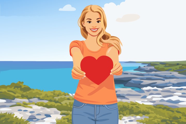 Smiling person holding out a small red heart towards the camera as a gift.