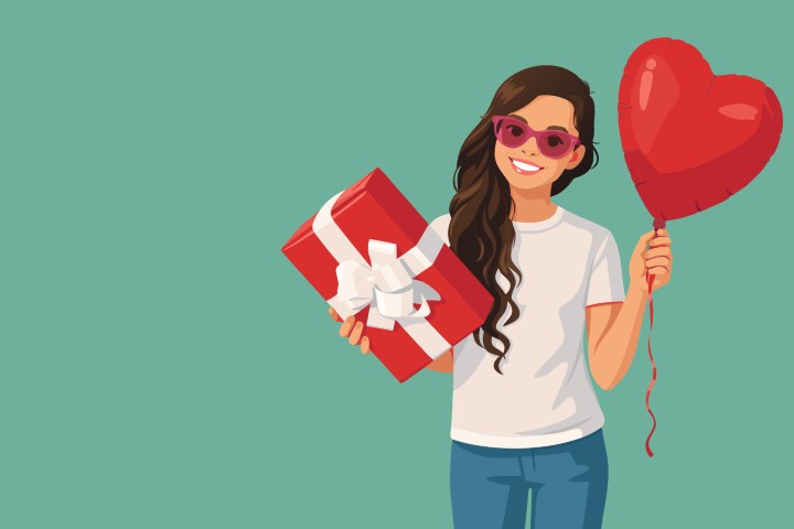 A stylish woman poses while holding a red gift box and a heart shaped balloon.