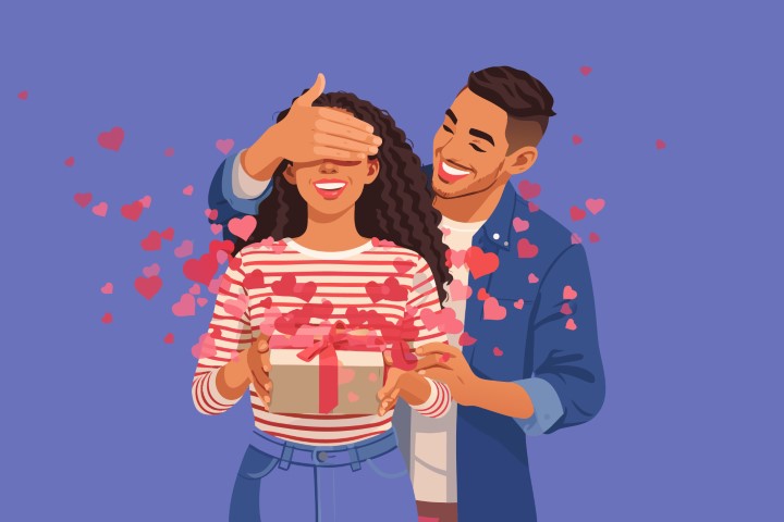 A man surprises his partner by covering her eyes while she holds a gift.