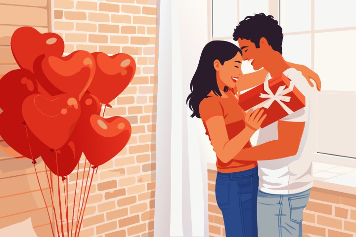 A joyful couple stands surrounded by many red heart balloons in a bright room.