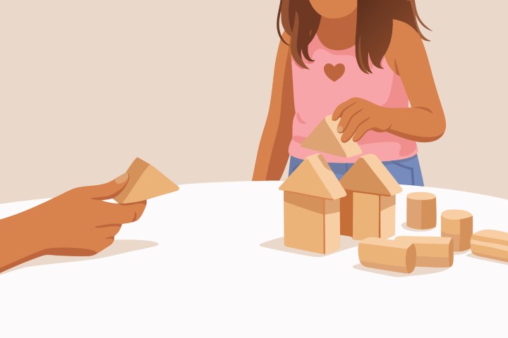 Child building a tower with wooden blocks on a white table.