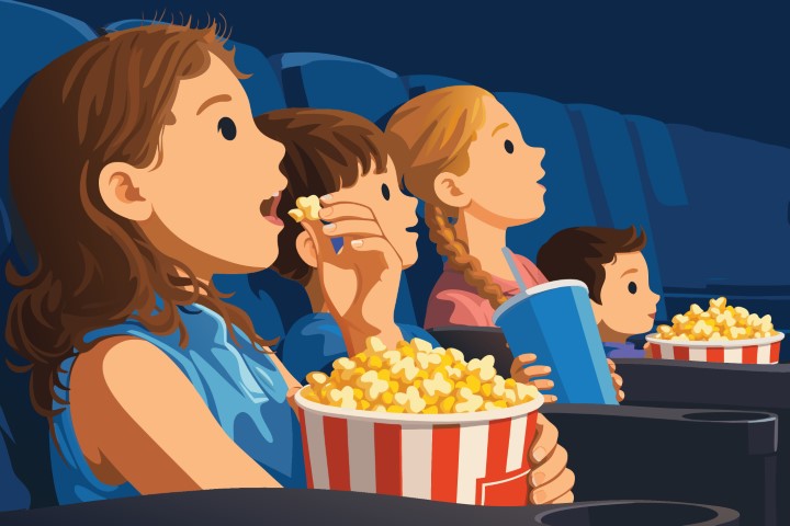 Family watching a movie in a dark cinema theater eating popcorn.