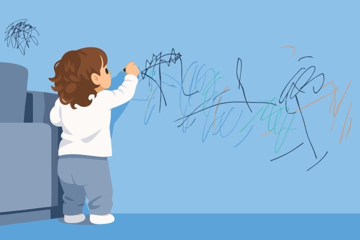 Young child standing in a room and drawing freely on a large blue wall.