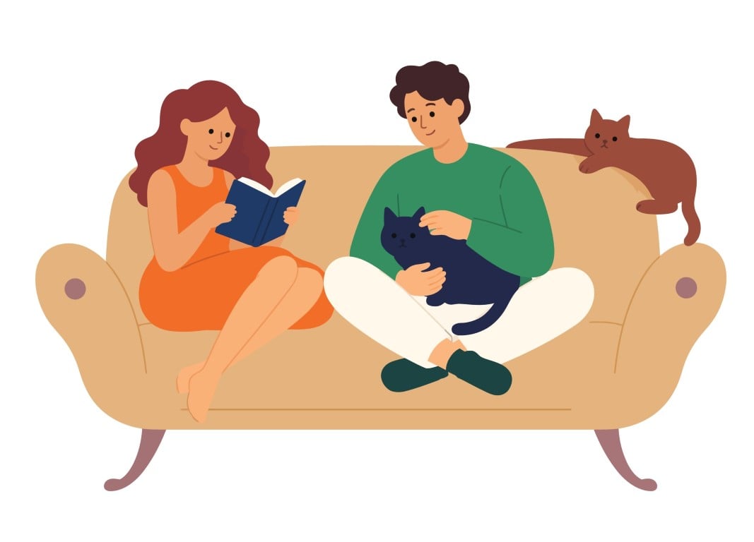 Couple relaxing on a sofa at home with their two cats in a cozy living room.
