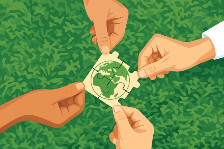 Hands holding a green world map icon over green grass.