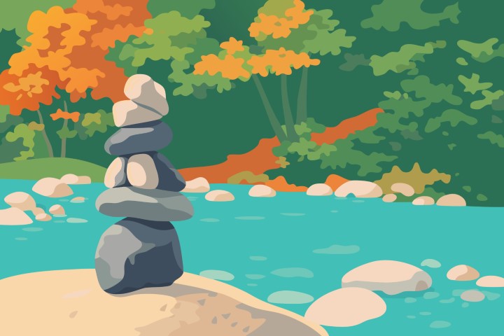 Stacked zen stones by a river in a beautiful autumn forest landscape.
