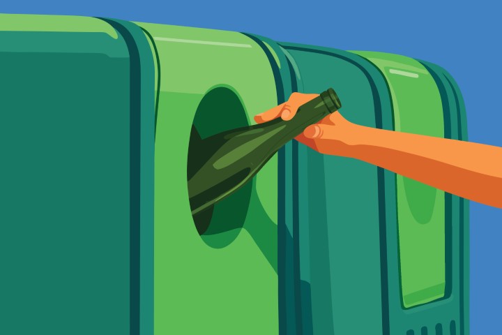 Hand putting a glass bottle into a green recycling bin for environmental protection.