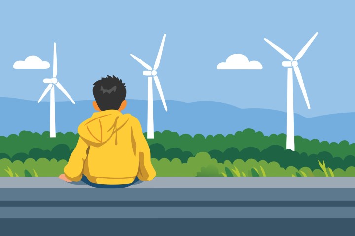 A child sitting alone watching wind turbines in a green field.